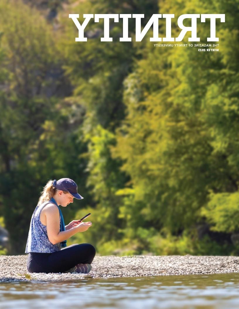 《2023年冬季三位一体》杂志的封面是一个人坐在靠近水的岩石上，通过放大镜观看